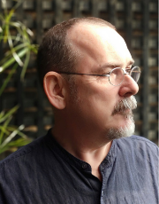Portrait of Prof. Peter Keogh. He is looking off to the right of the picture. He has short dark hair and a goatee style beard and moustache, he is wearing wire framed glasses.