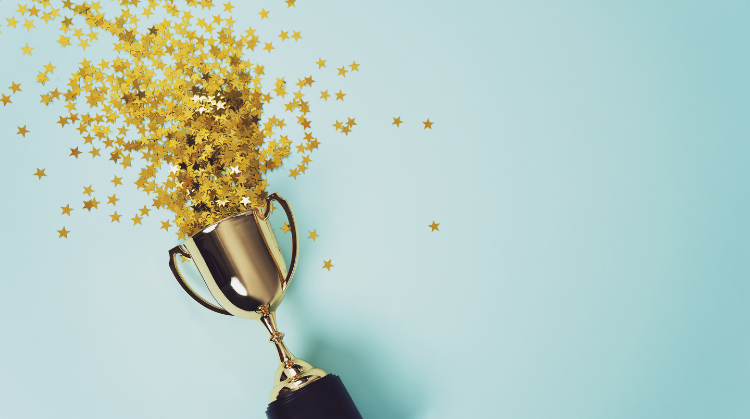Image of little gold cup with star confetti pouring out onto a blue background, concept for winning or success