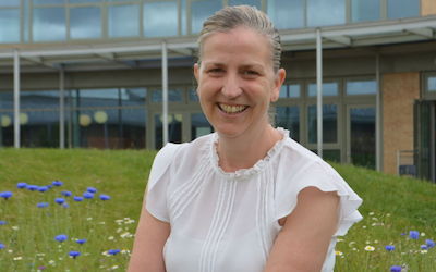 Portrait of OU Education Studies student Aimee Durning. She sits in a meadow garden outside her school.