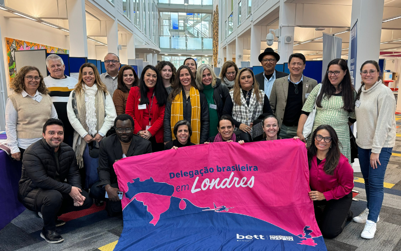 A group of the Brazilian delegates are pictured in the OU's Library. They are displaying a vibrant pink and blue flag with the words Delegacao brasileira em Londres