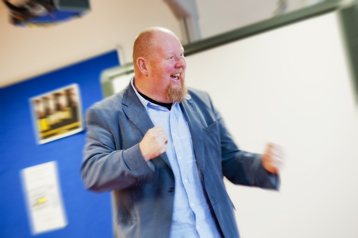 Stuart Wroe stands with his hands clenched in jubilant fists. He is smiling. The image around Stuart is slightly blurred showing movement.