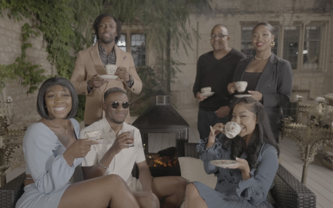 A group of 6 black men and women, sitting in a lounge area, drinking tea together. Image credit- Cardiff Productions