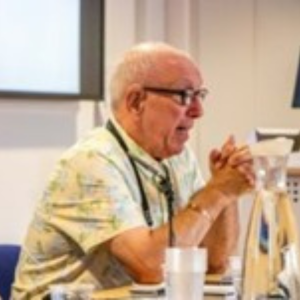 Ian Davies speaking at a conference with his hands clasped together