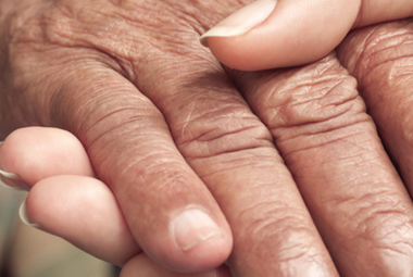 A young hand with long, manicured nails holds an older, wrinkled hand