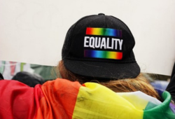 Photo of someone wearing a baseball hat saying "equality" and wearing a rainbow flag