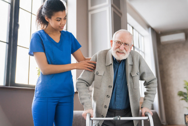 A nurse helps an elderly man to walk with a zimmer frame