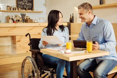 Woman in a wheelchair showing something to a man.