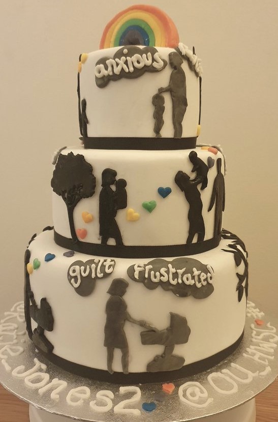 Katie Jones' cake is shown. It is a 3-tier cake iced in white with a rainbow on top. Piped words around the cake read, 'anxious', 'guilt', 'frustrated'. Silhouettes of parents and children from birth to toddler are attached to the sides of each tier in dark brown fondant icing.