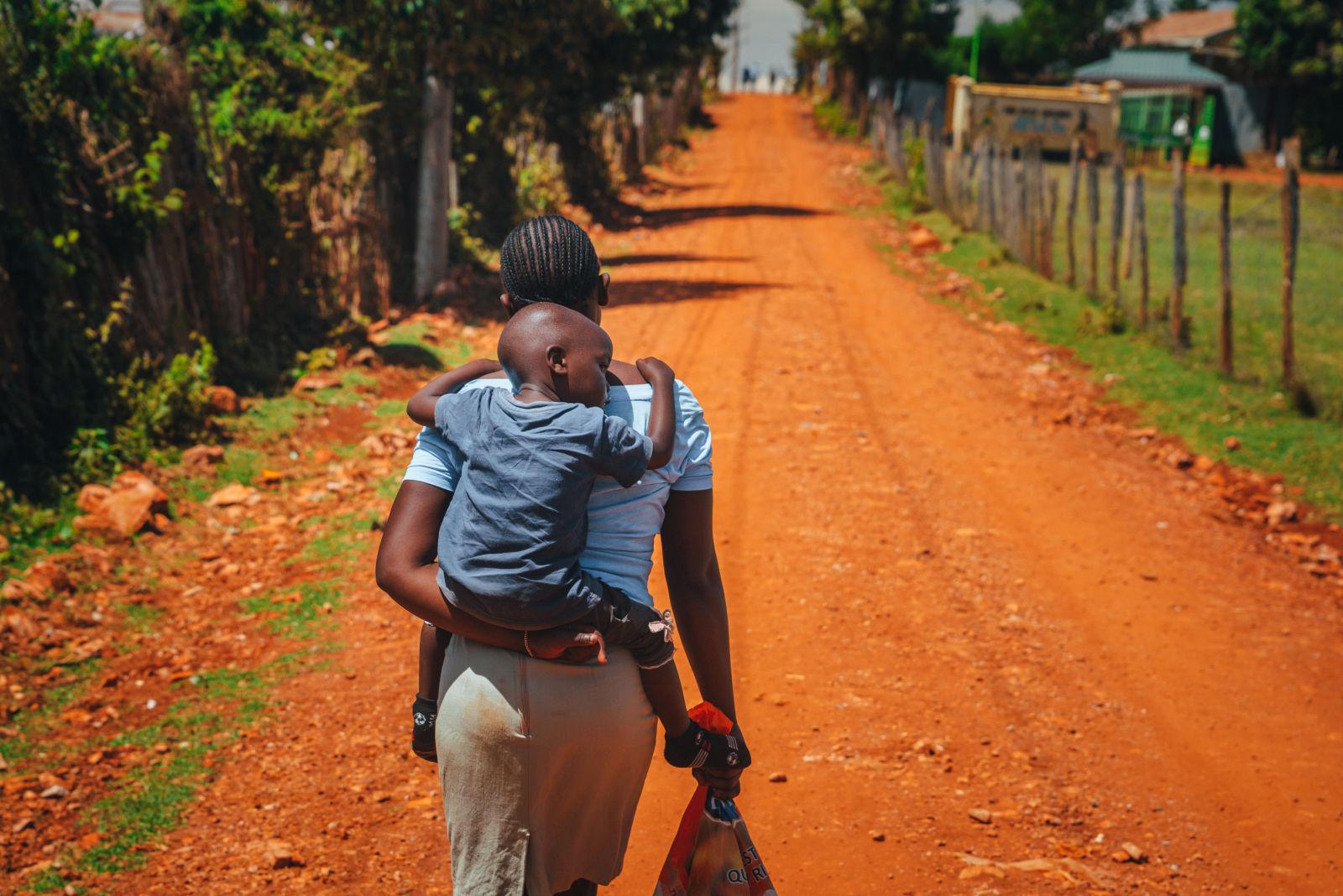 Image of a woman carrying a child on her back while walking