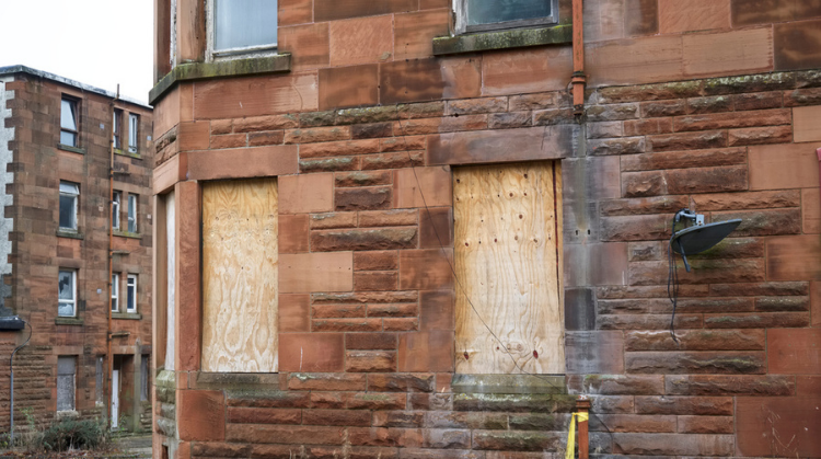 Red brick residential buildings are shown in a state of dereliction, with boarded up windows.