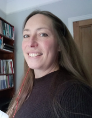 Portrait of Professor Kristina Hultgren. She is side on to the camera, looking into the lens and is smiling. She has long brown hair and is wearing a headset- you can just see the red cable from the headset. 