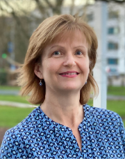 Portrait of Professor Joan Simons. She is looking at the camera and smiling. She has shoulder-length dark blonde hair and is wearing a blue print top. 