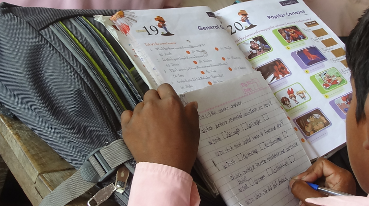 a young boy is writing in English in his exercise book whilst reading a school text book