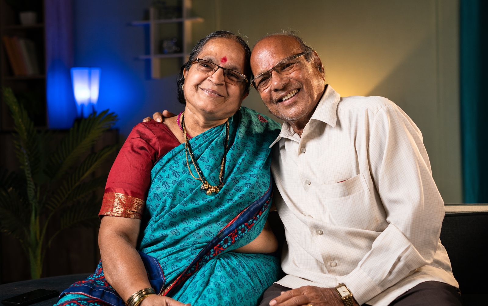 Portrait shot of a happy senior couple embracing each other by looking camera at home showing the concept of relationship, happiness and family bonding