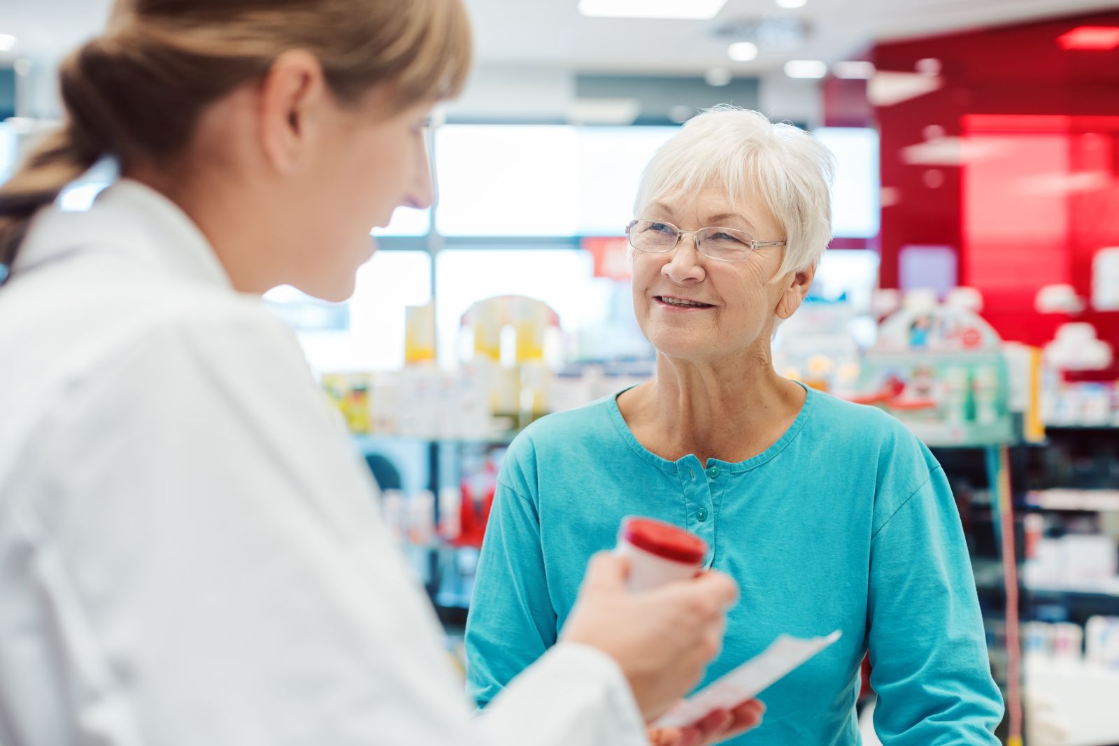 Senior woman in pharmacy talking to the chemist or pharmacist explain effects of a drug