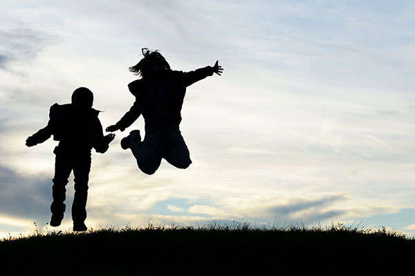 Silhouette style picture that shows to kids jumping in the air.