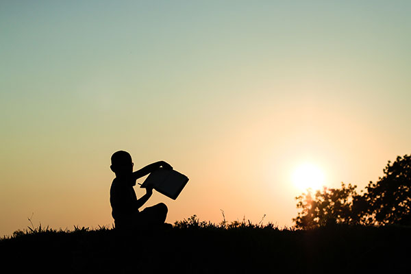 Silhouette style picture that shows a kid holding a book open and trying to write something.