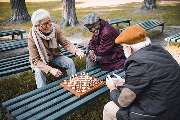 a multiethnic group of three old men playing chess in a park