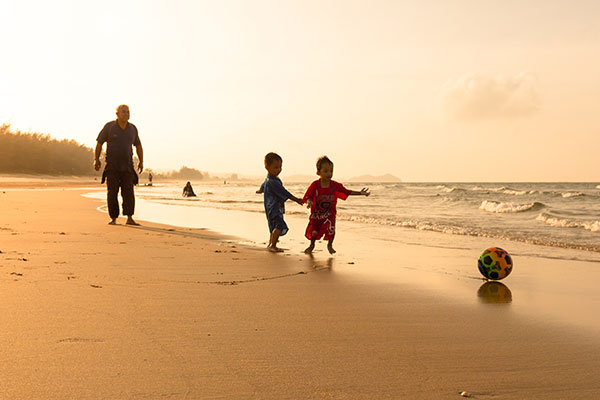 an old man playing football with two children on the beach