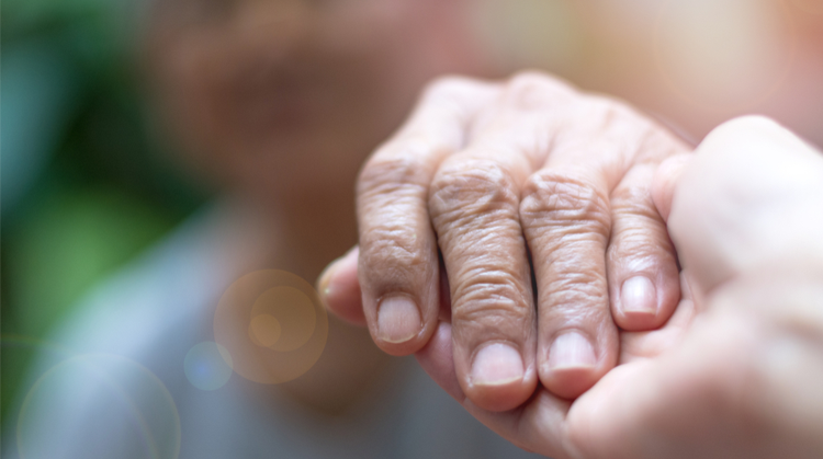 Two hands are pictured in focus with the background blurred. The older hand is being held by a younger one. 