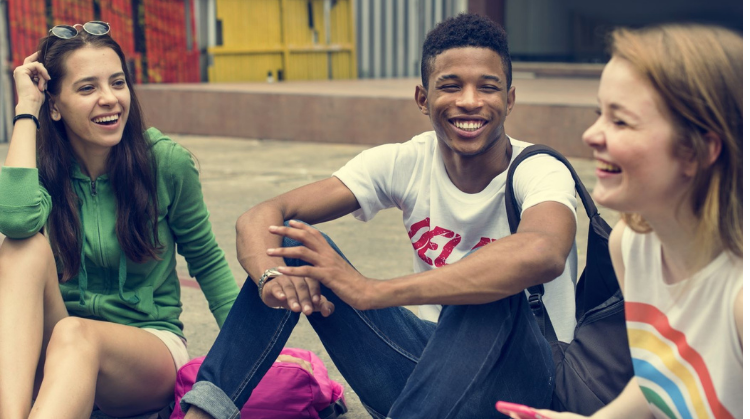 Three teenagers sit outside chatting and laughing together.