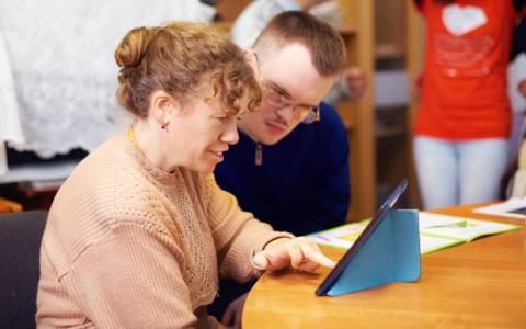 Two young adults with learning disabilities study something on a tablet screen.