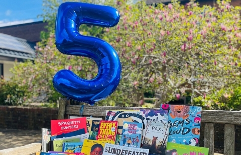 A shiny blue helium balloon in the shape of a 5 floats above a display of books.