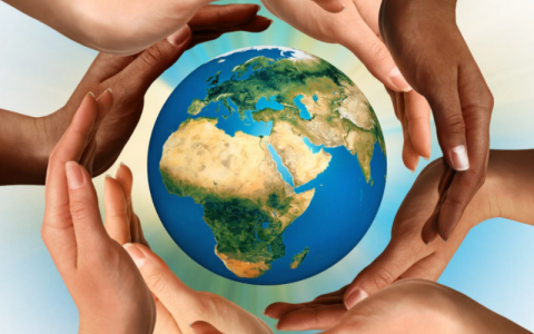 Eight hands of different ethnicities surround a 3D graphic image of the world in an overlapping circle. The globe is pictured with Africa, Asia and Europe in view.