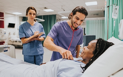 A nurse takes a patient's observations while a trainee nurse makes notes in the background