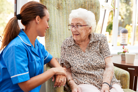 Senior woman sitting in chair laughing with a care professional in a care setting.