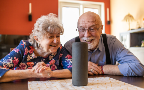 elderly couple sitting at a table at home, using a Virtual Assistant