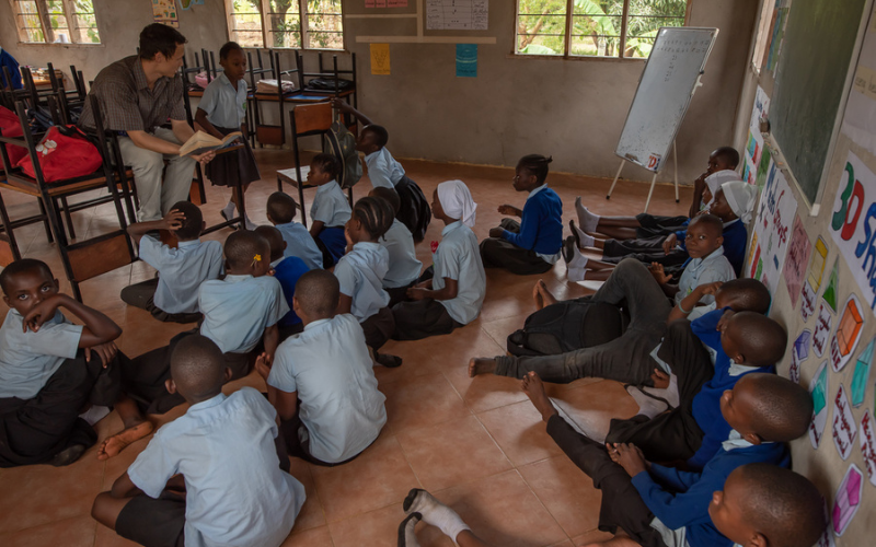 African school children sitting on the floor listening to a teacher reading a book