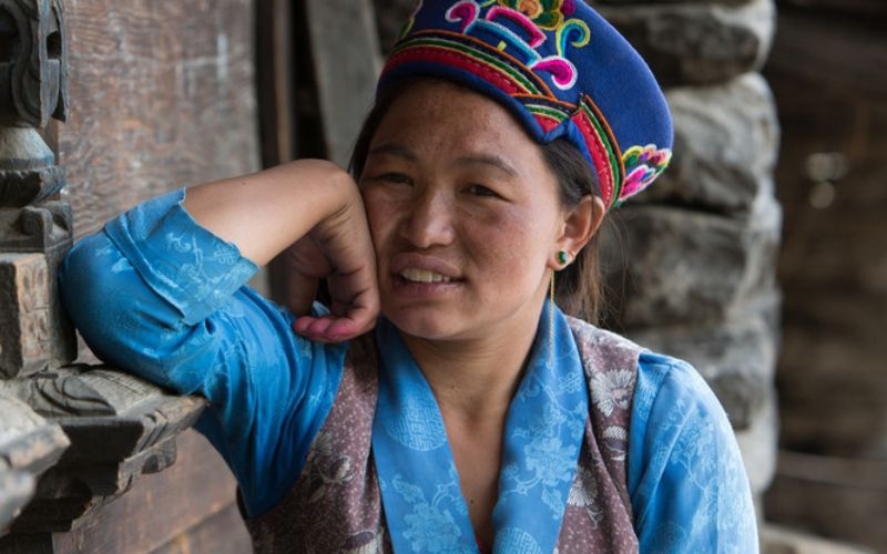 Young Nepalese woman dressed in blue wearing a colourful hat looking to the camera