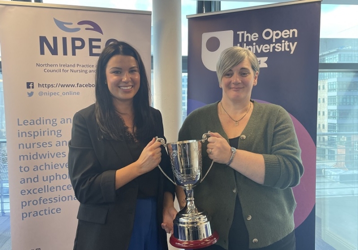 A photograph of OU nursing graduates Lucy Duke and Shelley Taylor pictured standing in front of an OU banner and an NIPEC banner with their award.