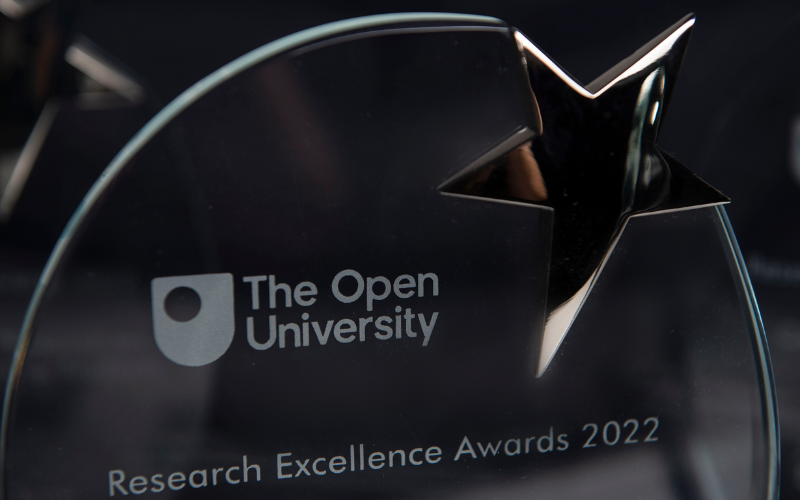 Close up of an oval glass trophy with a silver star attached. On it is etched the OU log and text which reads The Open University, Research Excellence Awards 2022. 