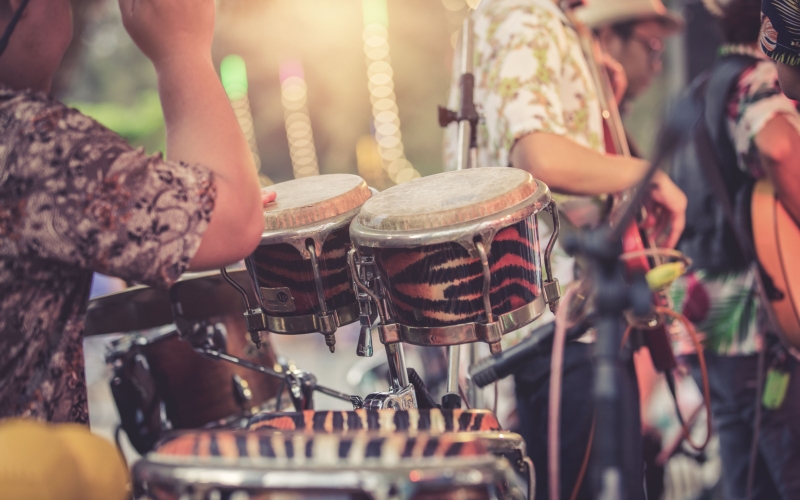 Close up of man playing drums in the foreground with three performers in the background
