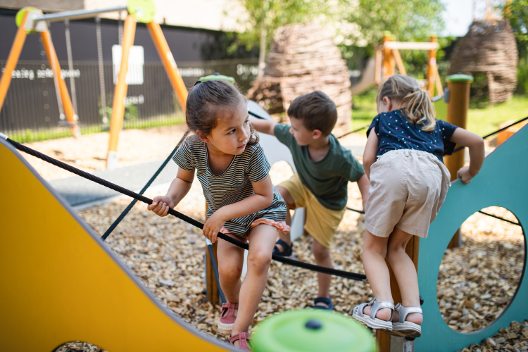Three small children playing together outdoors in a nursery playground