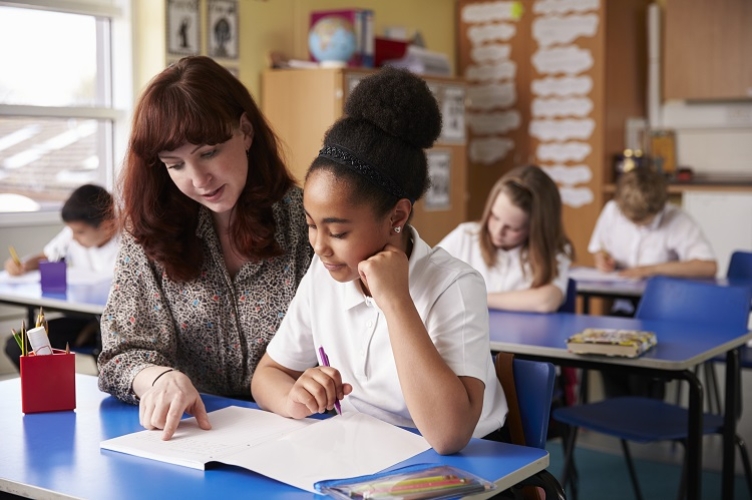 A photograph of a teacher helping a young student with their class work in a school environment.