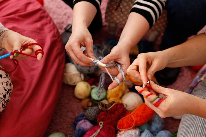 a close up of a group of people's hands knitting colourful yarn together